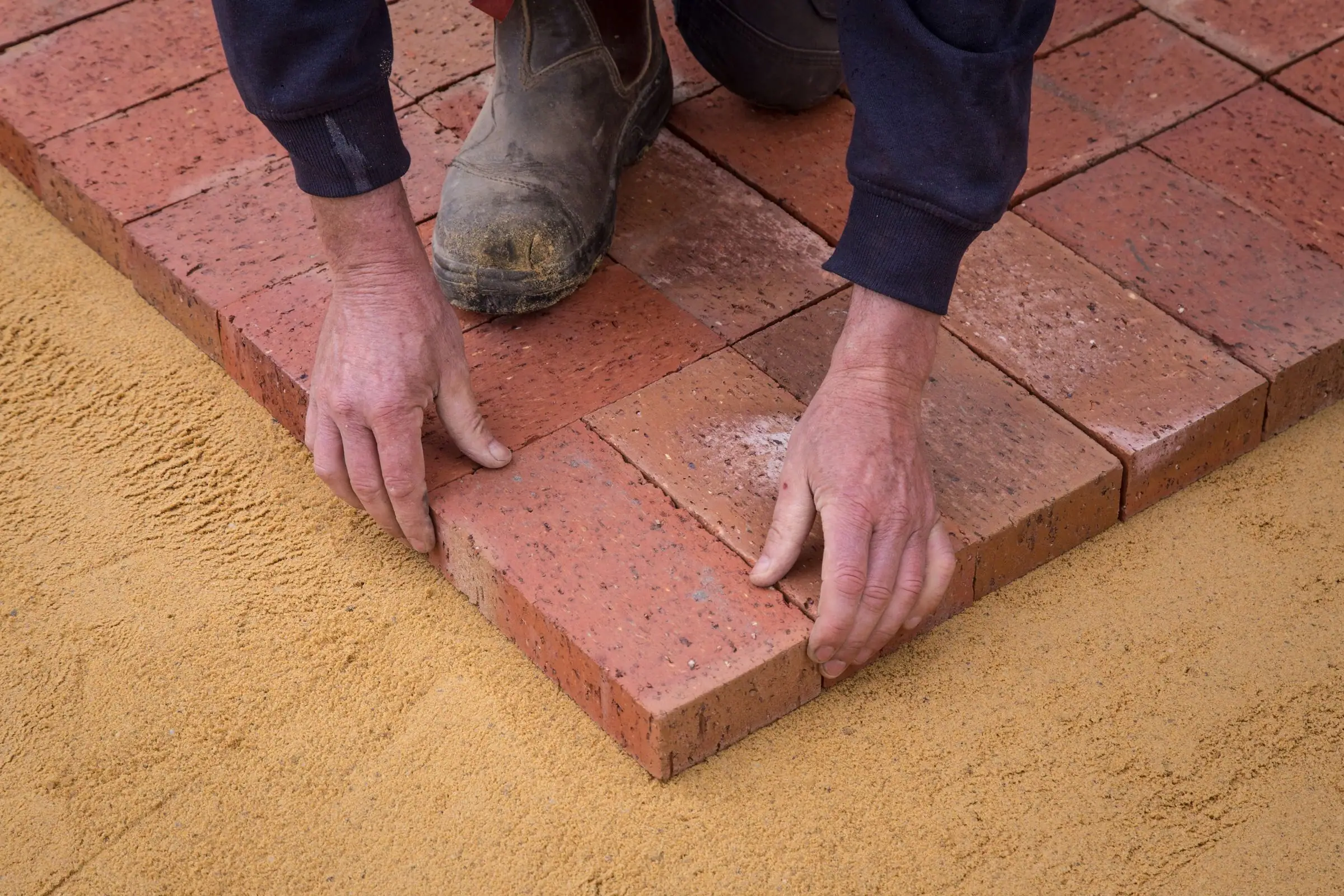 Hands setting brick pavers on a sand bed
